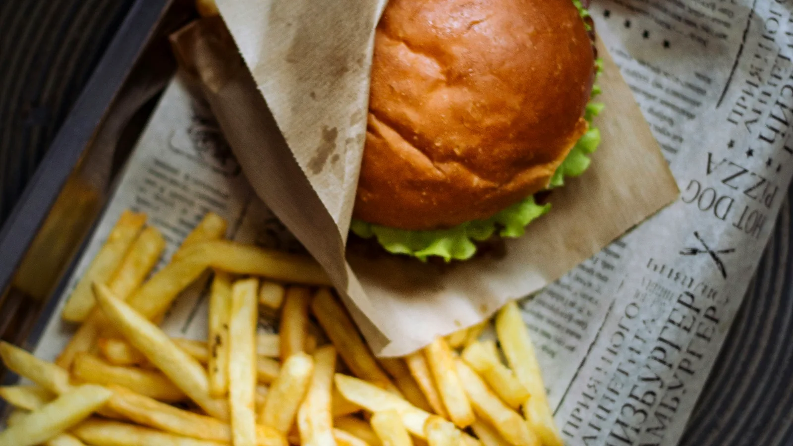 Hamburguesa envuelta en papel antigrasa sobre una bandeja con papas fritas