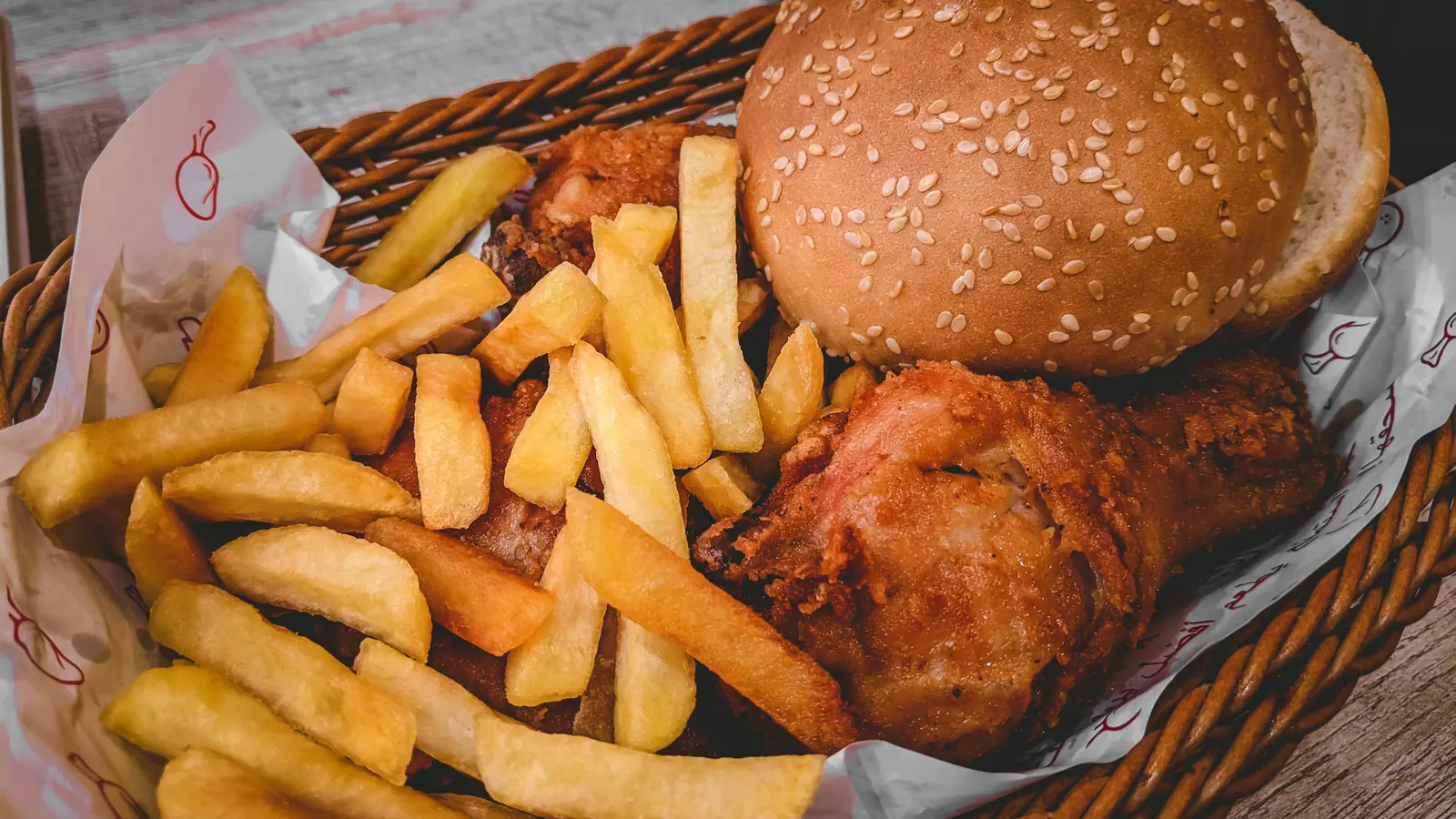 Hamburguesa, pollo apanado y papas servidos en una canastilla forrada con papel antigrasa impreso